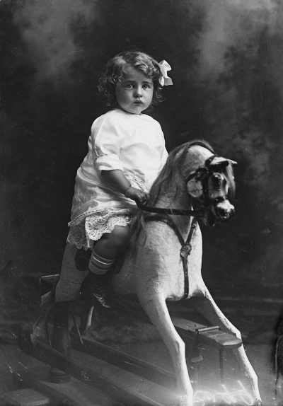 Studio portrait of a girl on a rocking horse.  Family name Rugg.