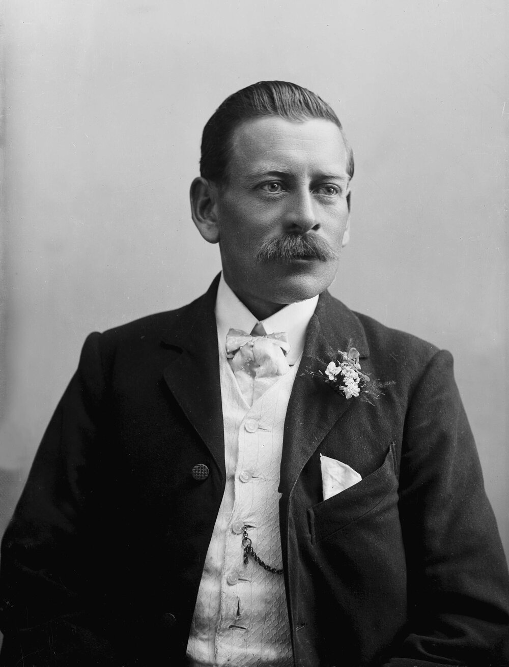 Studio portrait of a moustached man wearing a white waist-coat.