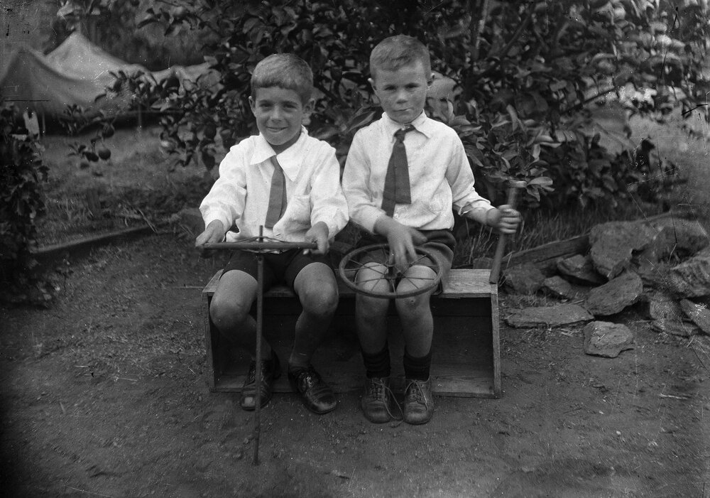 Two unidentified boys seated together on a wooden box.