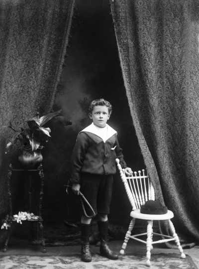 Studio portrait of a standing boy who holds a whip.  Family name Johnson.