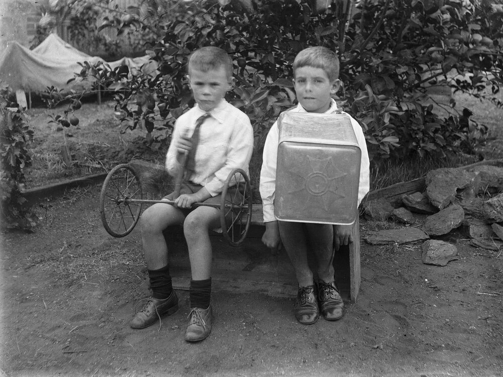 Two unidentified boys seated together on a wooden box.