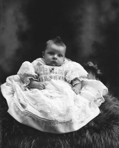 Studio portrait of a baby seated on a fur rug.   Family name Cook.