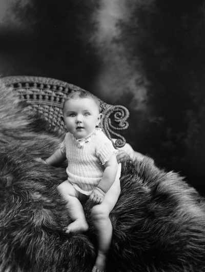 Studio portrait of a baby seated on a fur rug.  Family name Cutts.