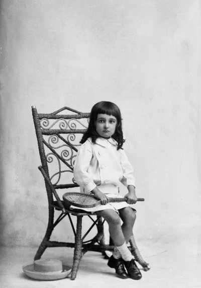 Studio portrait of a seated young girl holding a racquet.   Family name McKinnon.