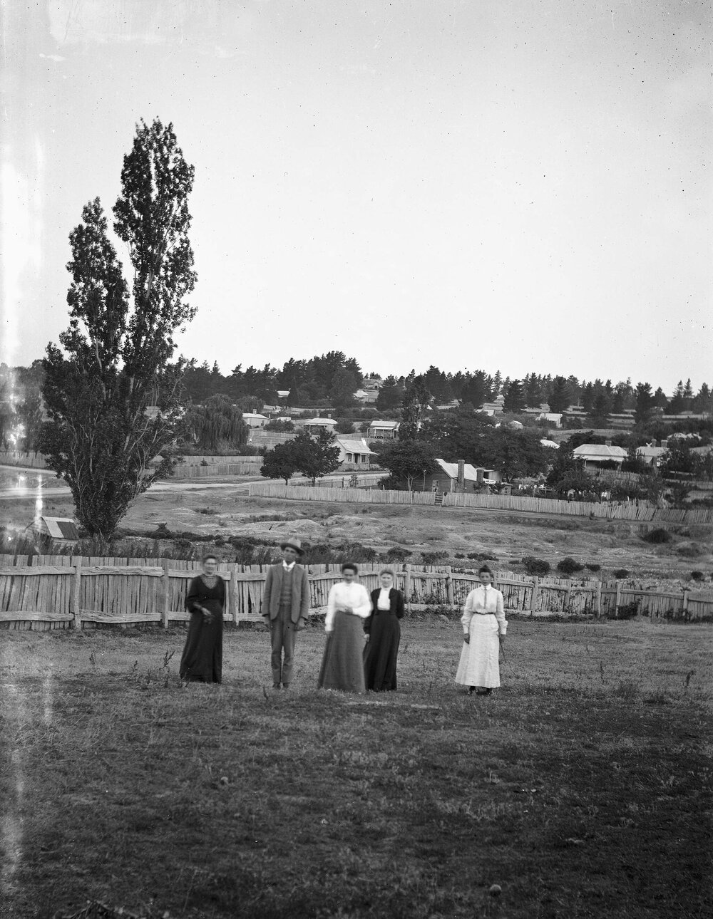 An unidentified group of people in a paddock with a town in the background..