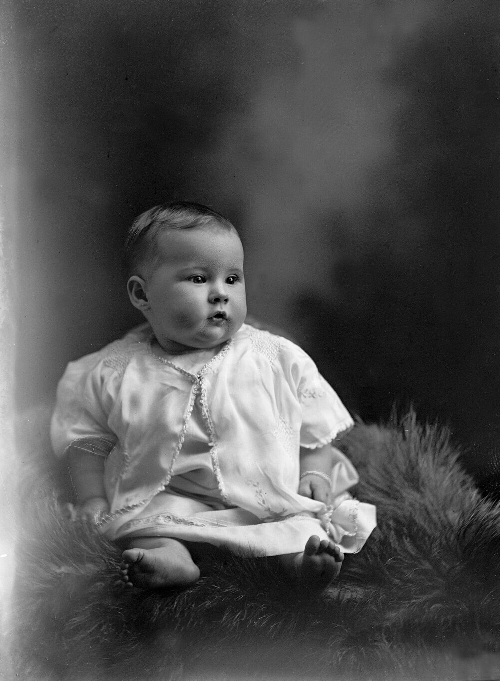 Studio portrait of a baby seated on a fur rug.  Family name Rowell or Howell.