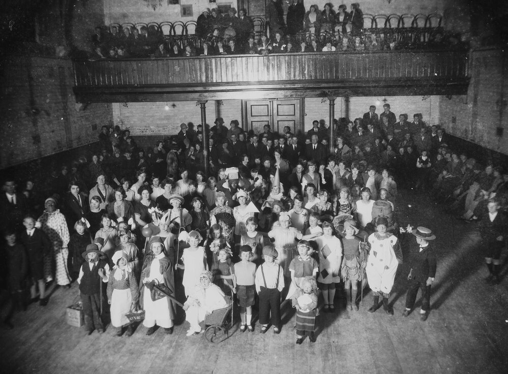 A large hall crowded with children in fancy dress costumes and adults in the background.