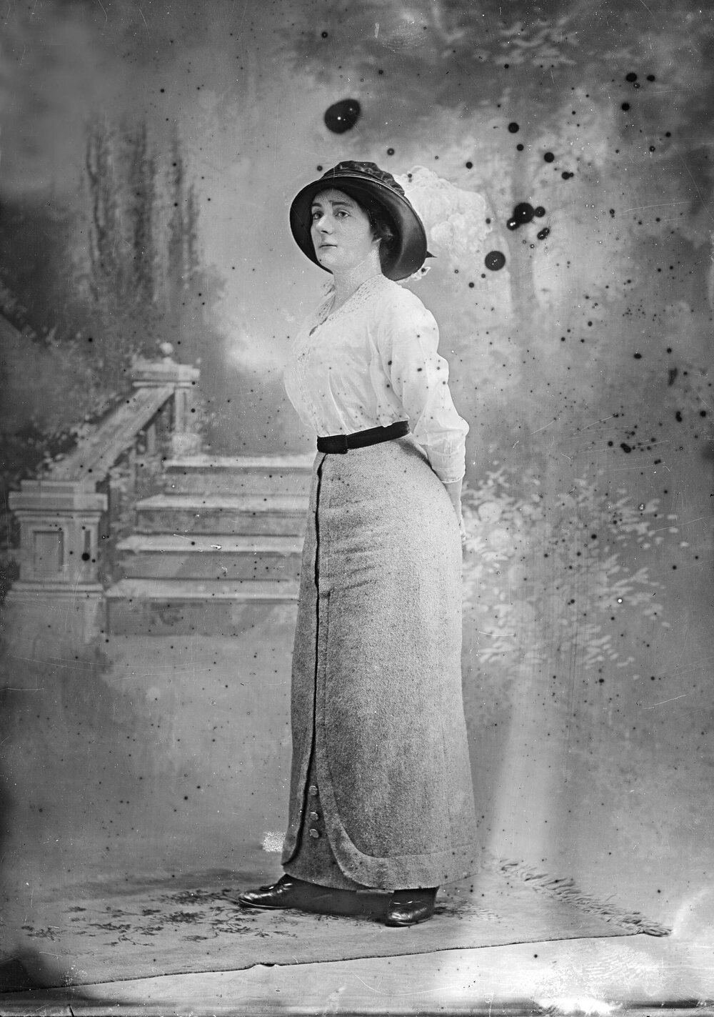 Studio portrait of a woman wearing a hat and long skirt.