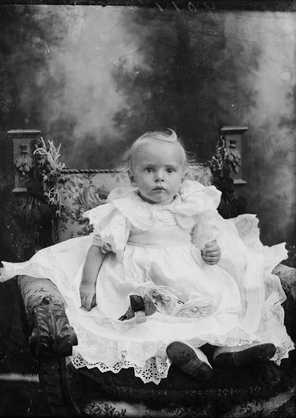Studio portrait of a baby seated in an elaborate chair.