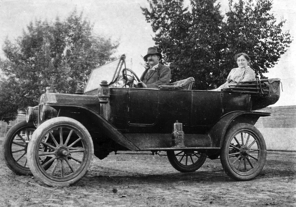 An open touring car with male driver and female passenger.