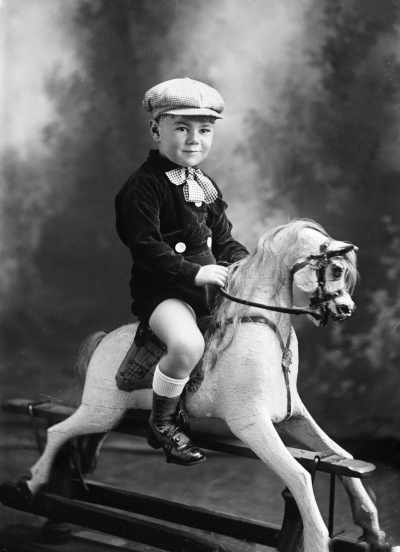 Studio portrait of a young boy seated on a rocking horse.  Family name Rogers.