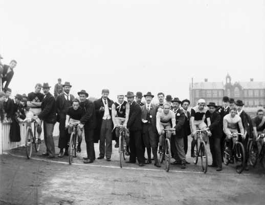 Seven cyclists with supporters and onlookers.