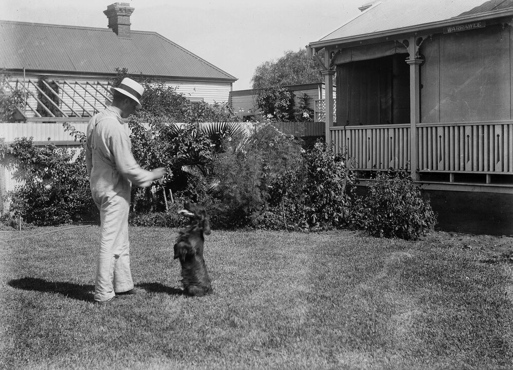 An unidentified man playing with a dog in front of a house named Warrawee.