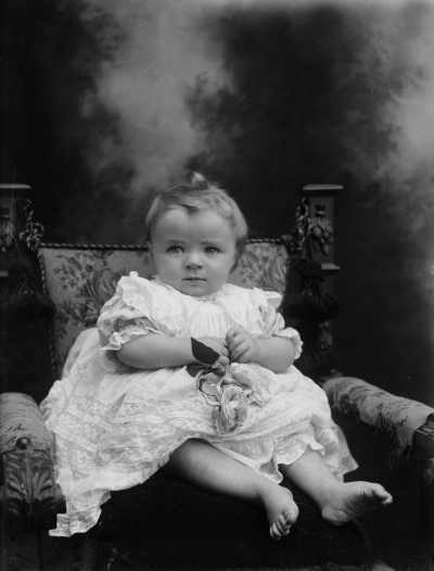 Studio portrait of a  baby wearing an elaborate dress.  Family name Gibson.