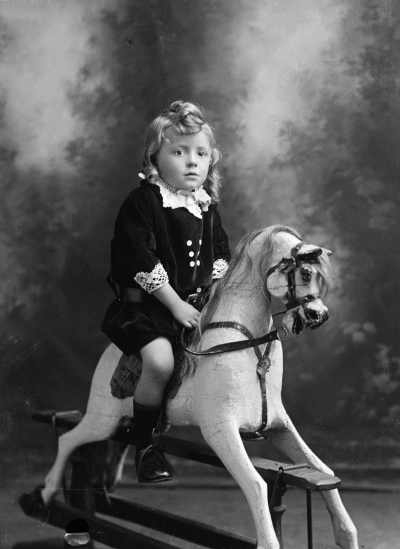 Studio portrait of a girl on a rocking horse.  Family name Fisher.