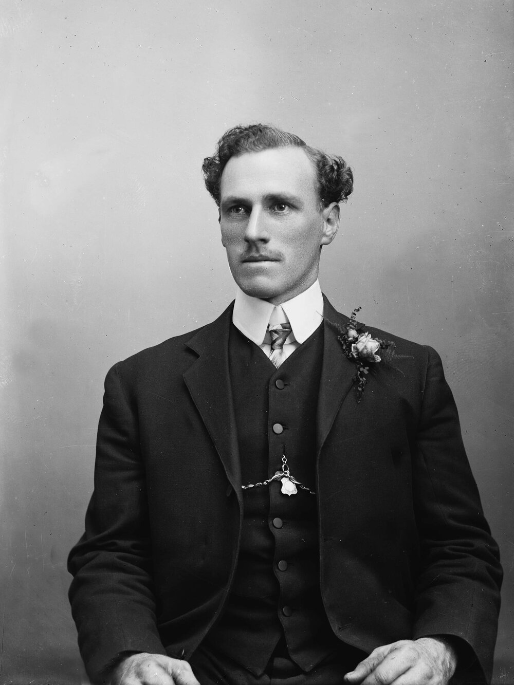 Studio portrait of a man wearing a button-hole spray of flowers.  Family name possibly Stewart.
