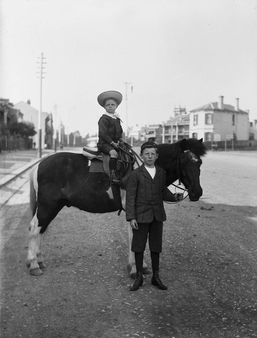 Two unidentified boys with a horse in an urban environment.
