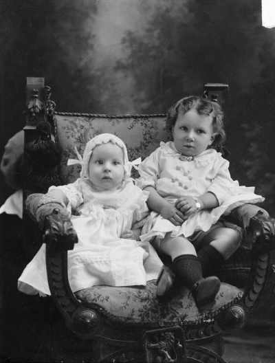 Studio portrait of a baby and a young child seated together.  Family name Price.