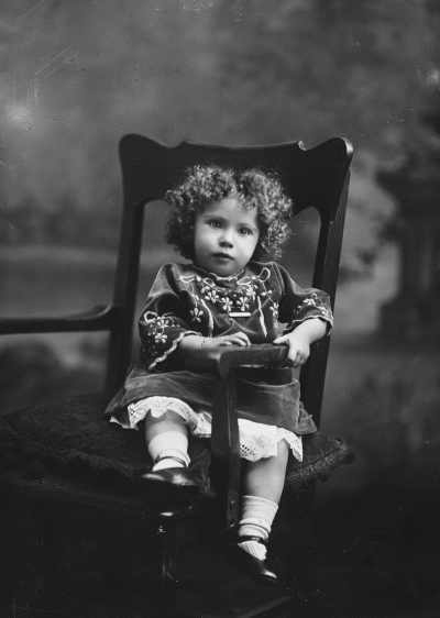 Studio portrait of a young girl in an embroidered dress.  Family name Bussell.