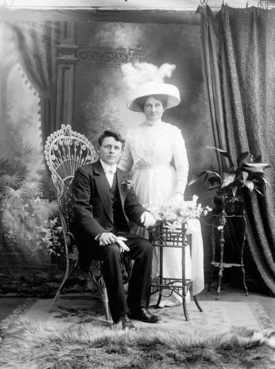 Studio portrait of a seated man and a standing woman holding flowers.  Family name Mc Coy.