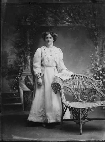 Studio portrait of a young woman standing at a wicker chair.