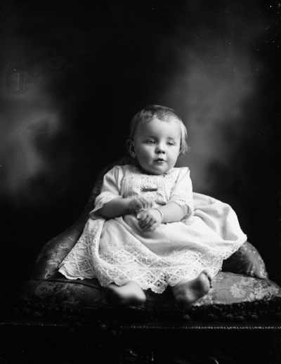 Studio portrait of a baby wearing a dress.  Family name Johns.