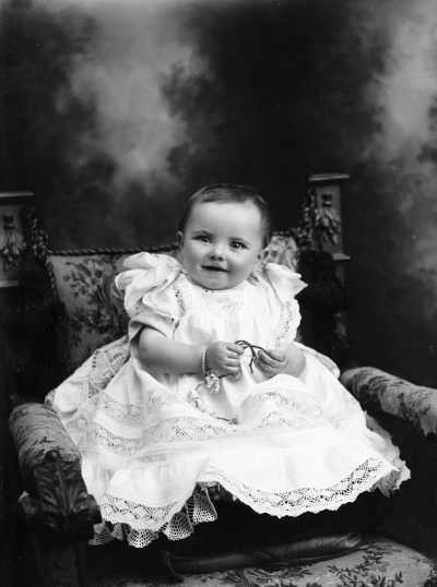Studio portrait of a baby wearing a dress.  Family name Carroll.
