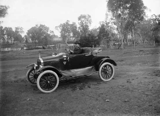 A man at the wheel of an open coupe car.