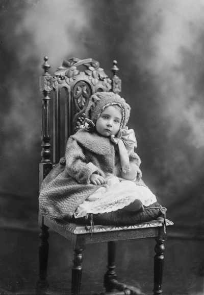 Studio portrait of a baby girl wearing a coat and hood.  Family name Winrow.