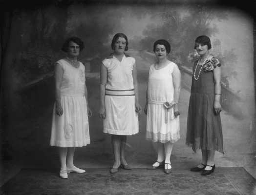 A group of four unidentified women in front of a painted studio background.