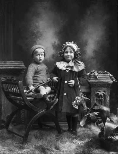 Studio portrait of a girl standing alongside a seated boy.  Family name Hardiman.