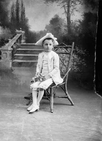 Studio portrait of a boy wearing a triangular hat and holding flowers.