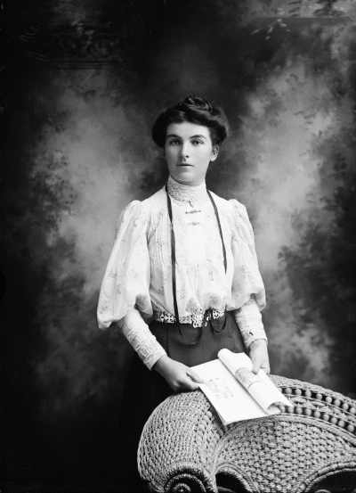 Studio portrait of a woman standing at a wicker chair.  Family name Roberts.