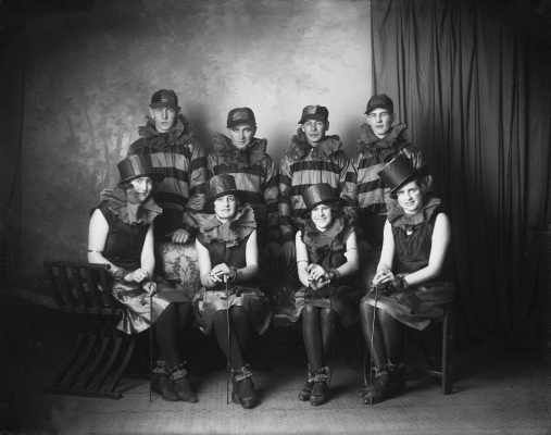 A posed group of four women and four men in matching theatrical costume.