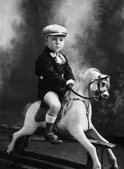 Studio portrait of a young boy seated on a rocking horse.  Family name Rogers.