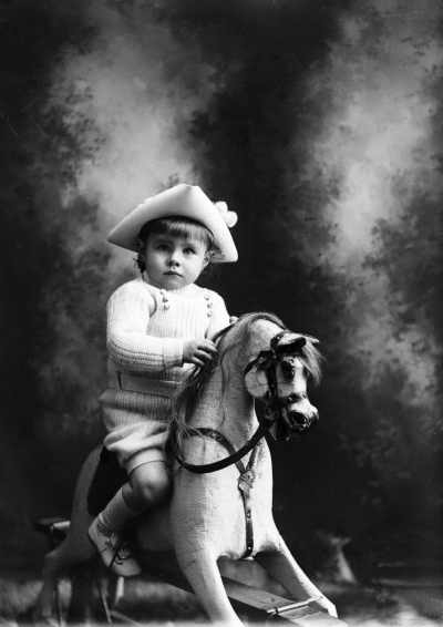 A studio portrait of a young boy siting on a rocking horse.
