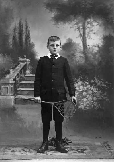 Studio portrait of a boy holding a stringed racquet.  Family name Merry.