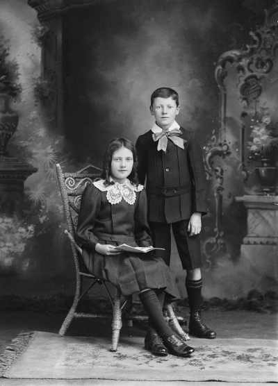Studio portrait of a boy standing alongside seated girl.  Family name Kuhl.