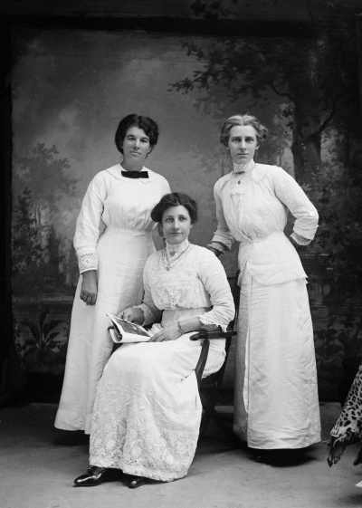 Studio portrait of three women wearing white dresses (one is possibly May Wilson).