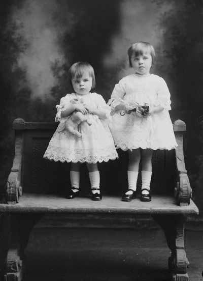 Studio portrait of two young girls standing on a garden seat.   Family name Groves.