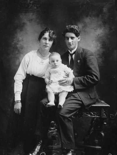 Studio portrait of a seated woman and man holding a baby.