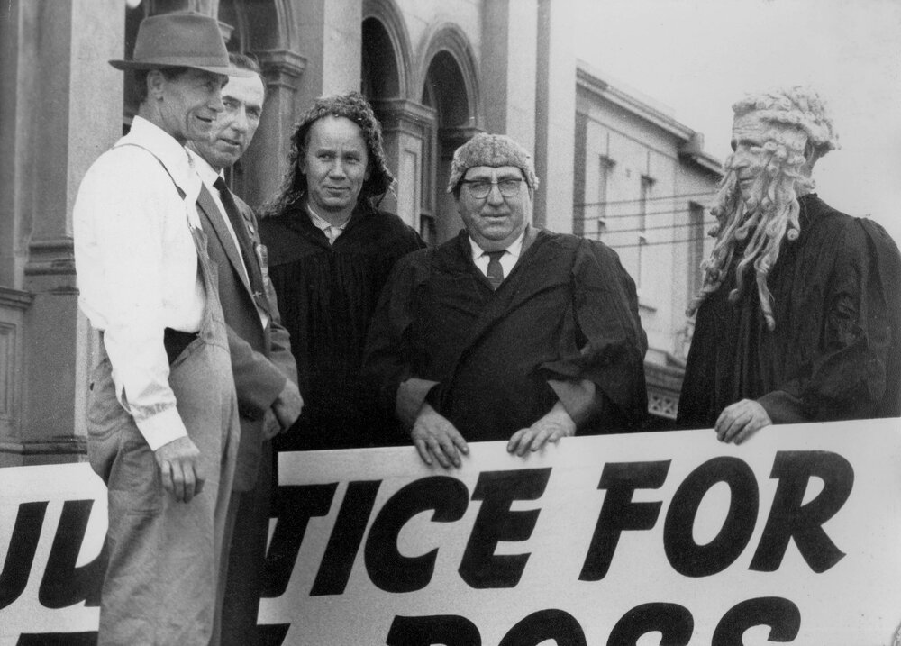 Trade unionists, some dressed in mock wigs and gowns, holding a protest sign.
