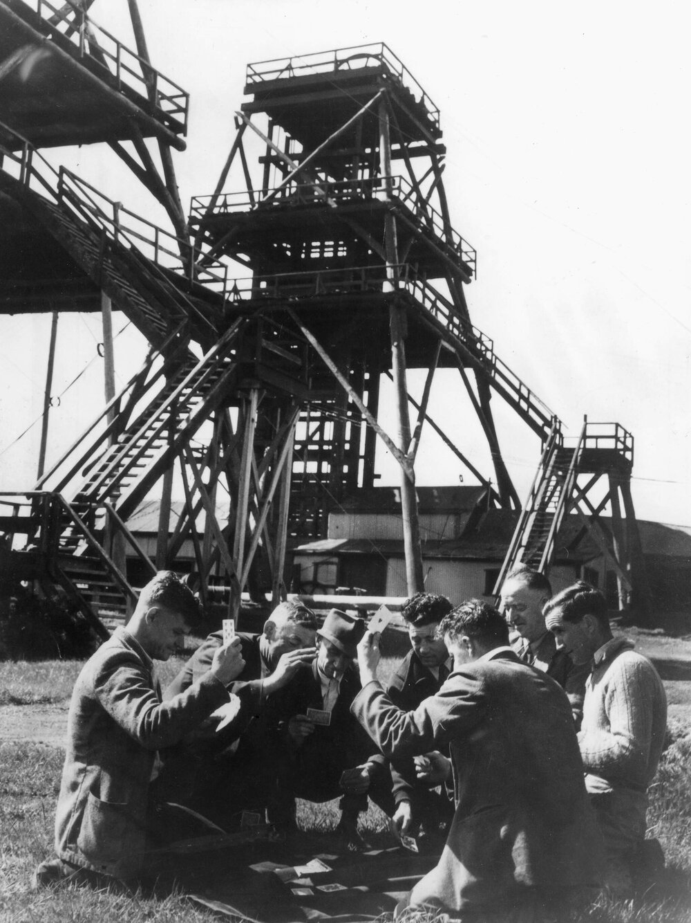 Miners playing cards in front of a poppet head at Wonthaggi, State Coal Mine, Victoria in 1949.