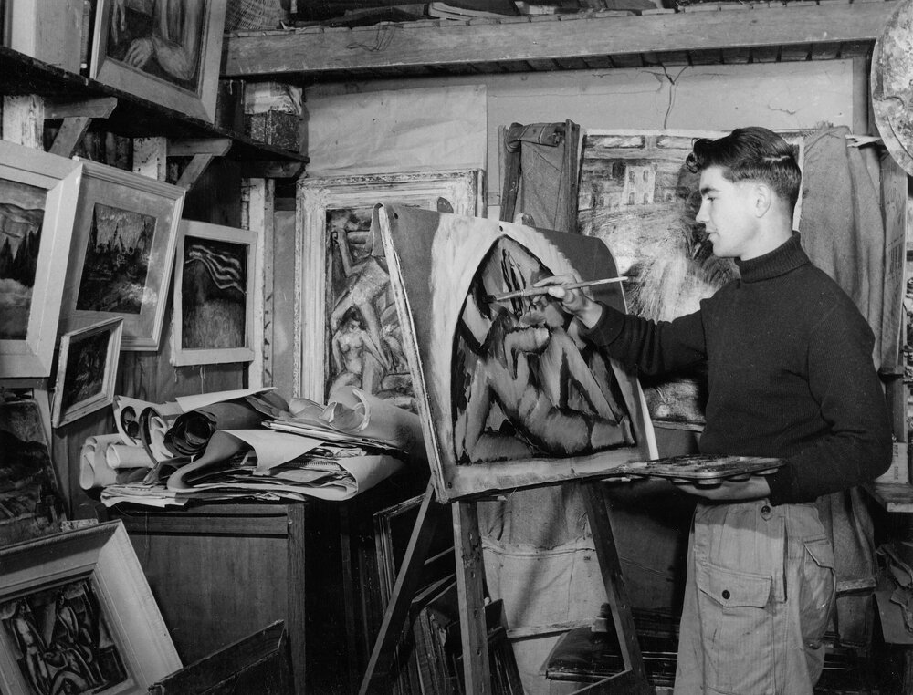 Portrait of Len [Leonard] French  painting in an artist's studio.
