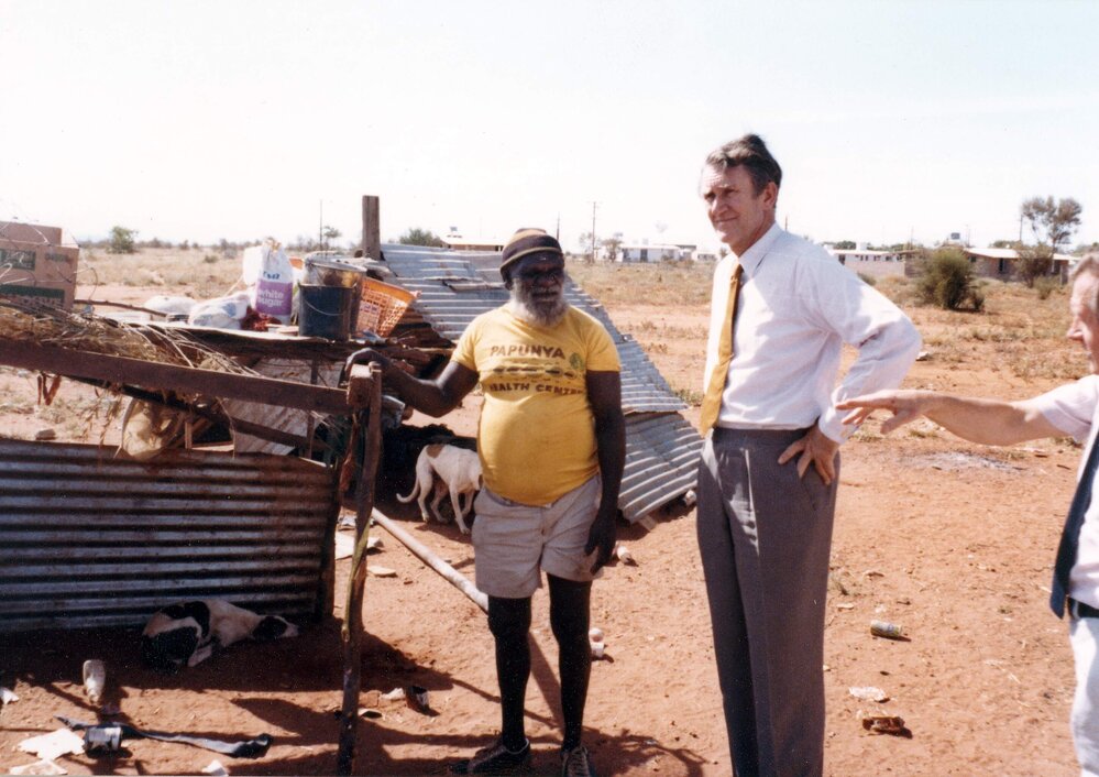Malcolm Fraser and an Aboriginal Australian man standing alongside a dwelling in the Northern Territory.