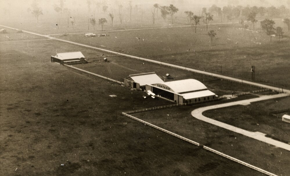 Aerial view of hangars and a biplane at an unknown location