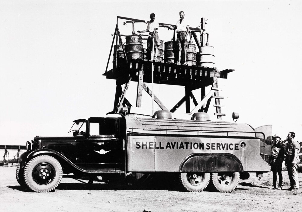 Two men standing on a high timber platform filling 44 gallon drums with fuel from a Shell Aviation Service Ford Sussex pump tanker in Darwin