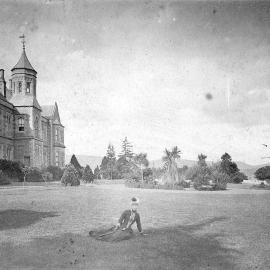 Woman seated on lawn in front of stately home