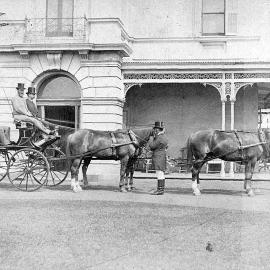 Photo of three men in horse drawn carriage, grooms attending horses