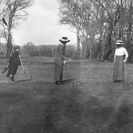 Photo of two women playing golf, and caddy